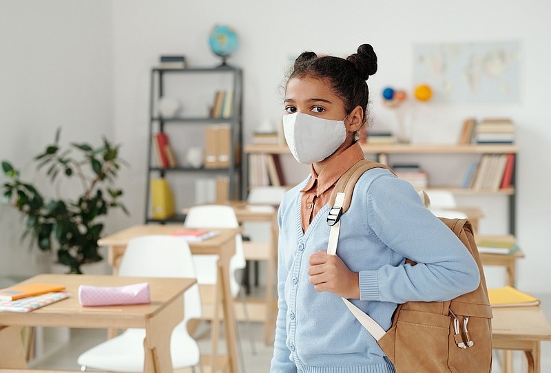 A student wearing a mask, carrying a back pack, prepares for hybrid learning