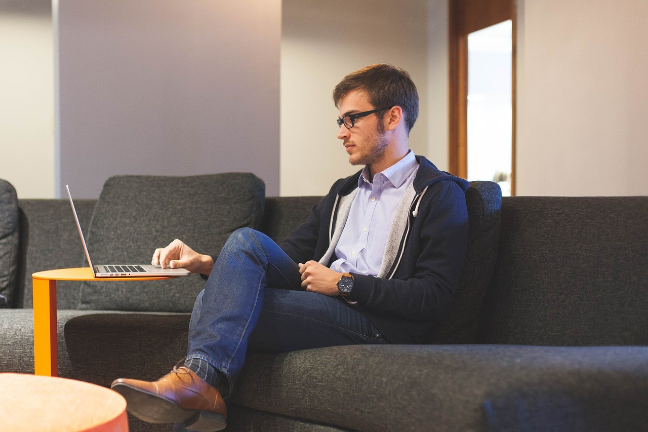 A young man sits on a sofa, studying the Meraki EA Pilot Program on his laptop